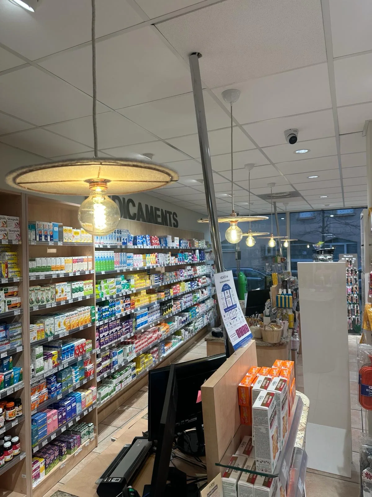 L'intérieur d'une pharmacie : luminaires suspendus neufs au-dessus des rayons de médicaments et caméra de sécurité fixée au plafond